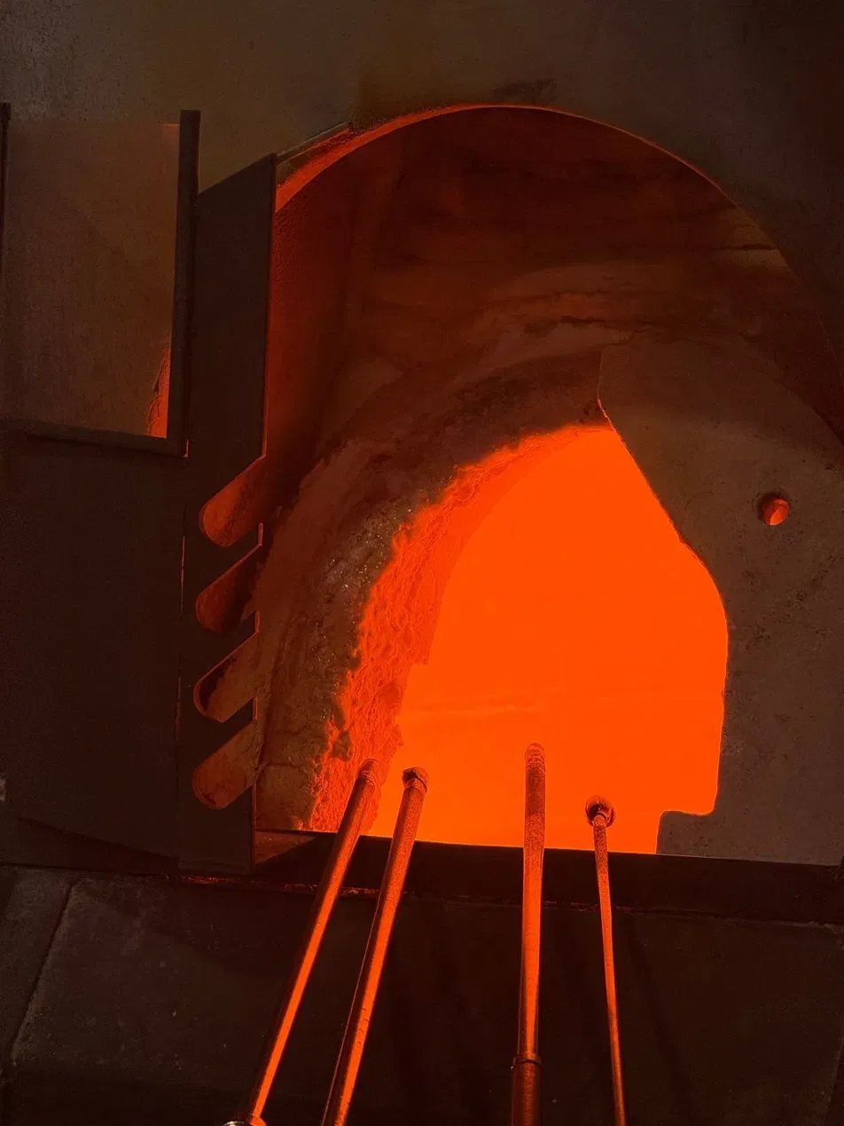 Glødende glasovn på glaspusteriet med glaspibernes ender i flammerne